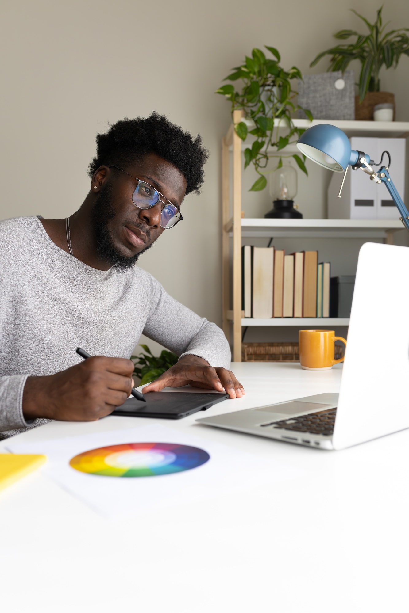 Black male graphic designer working at home using laptop and graphic tablet. Vertical image.